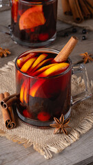 Mulled wine in glass mugs with spices and citrus fruit on an old wooden table. Copy space