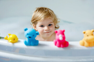 Adorable cute little toddler girl taking bath in bathtub. Happy healthy baby child playing with...