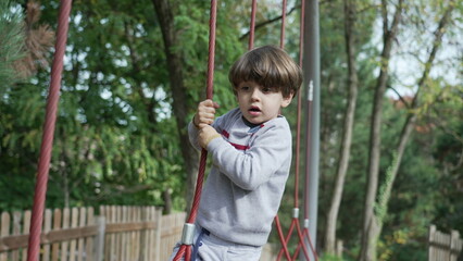 Obraz premium Playful little boy keeping balance at playground structure. Child playing at park exercising and being active