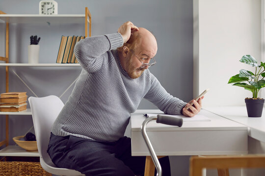 Senior man gets confused while doing a complicated task on a mobile phone. Old man scratching his bald head and looking at his modern smartphone with a puzzled face expression