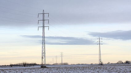 Electricity pylons along snow covered farm land under a colorful evening sky  in Munkzalm, Flanders, Belgium