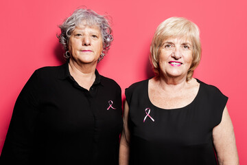 Positive elderly women with pink ribbons in studio