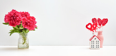 Red peonies in a vase and red heart on a white table with copy space. Mock up for displaying works. Valentine's day holiday background concept
