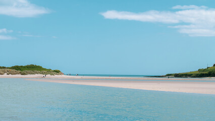 Clear cloudless sky over a beautiful sandy beach. A few people on a sandy beach. Picturesque seascape of Ireland on a summer day. A copy space. People walking on beach
