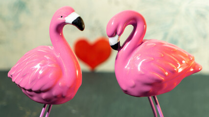 Couple of ceramic figurines of pink flamingos on background of heart and tropical pattern. Postcard...
