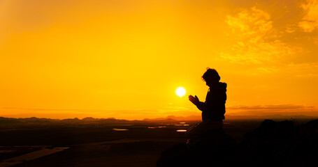 Fototapeta na wymiar Silhouette of a person praying at sunset on top of a mountain. Orange sky, religion concept. Copy space on the right