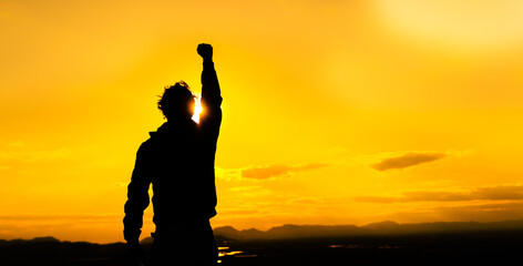 Man in silhouette at sunset with fist raised in protest. Protest concept. He is at sunset in a warm...