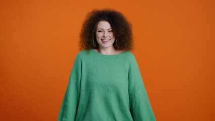 Attractive young woman in green knitted sweater, making delicious gesture over orange background