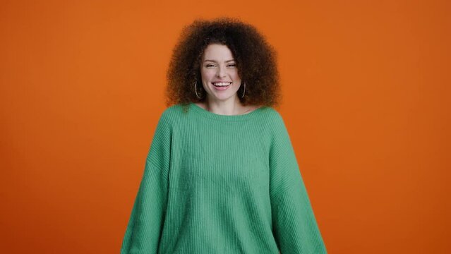 Attractive young woman in green knitted sweater, making delicious gesture over orange background