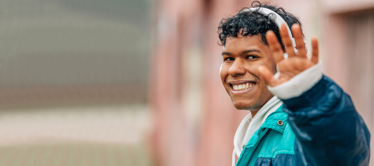 young latin man with headphones on the street waving