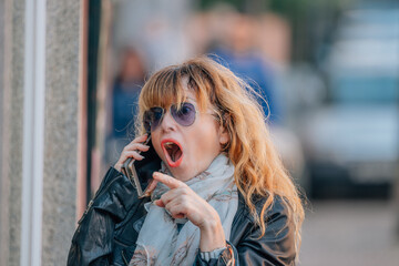 middle-aged woman in the street with mobile phone and expression of astonishment or surprise