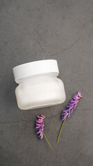 White bottle for cosmetics made of matte glass on  concrete background. Purple flowers. Minimalism in photo. Mok Up For Cosmetics, Mok Up For Designers, Product Advertising 