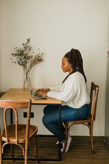 Cheerful african american woman using laptop while sitting on chair in living room - student, video call and working at home concept