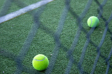 tennis balls on an artificial grass paddle court seen behind a fence