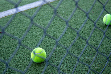 tennis balls on an artificial grass paddle court seen behind a fence