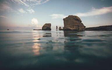 Woman paddleboarding through passage between sea rocks