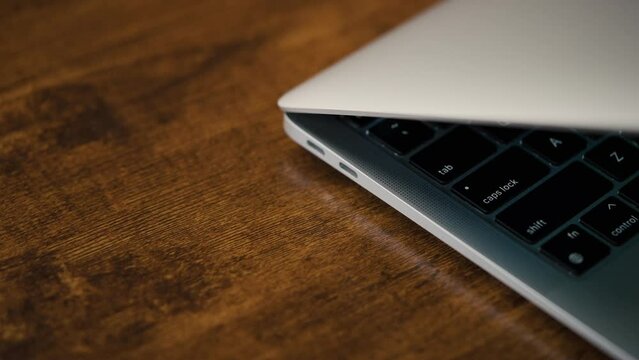 The laptop is lying ajar on the office desk. Close-up. Shift, Tab, Caps Lock keys in the frame. USB-C thunderbolt ports on the side panel.
