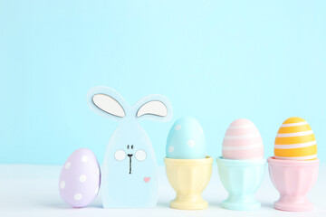 Colorful easter eggs in stands and wooden rabbit on blue background