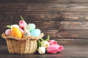 Colorful easter eggs in basket, egg in shape of rabbit and flowers of tulips on dark brown wooden background