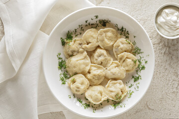 Plate of boiled dumplings with sour cream sauce on white textured background