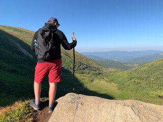 The traveler stands on the top of the mountain. Concept: climbing, hiking in the mountains. A tourist with a backpack behind his back looks into the distance.