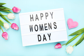 Flowers of tulips, pink felt heart and lightbox with text Happy Women's Day on blue background