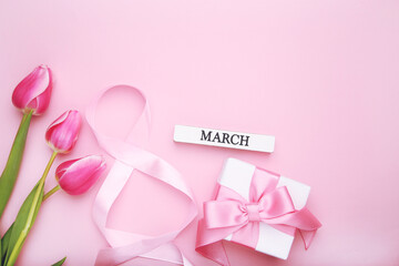 Ribbon in shape of figure number 8, gift and tulips flowers on pink background