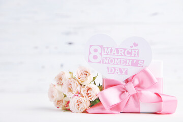Bouquet of roses, gift and card in shape of heart with text 8 March Women's Day on white wooden background