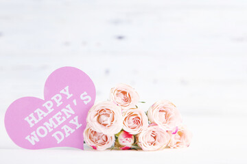 Bouquet of roses and card in shape of heart with text Happy Women's Day on white wooden background