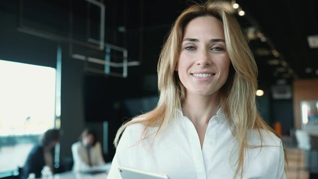Happy blonde female employee looking at the camera while standing in the office with colleagues