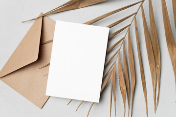 Blank greeting or invitation card mockup with natural palm leaf and envelope, card with copy space