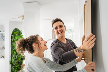 man and woman caucasian couple hanging painting on the wall at home