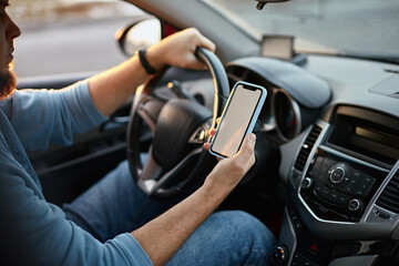 Man driver using mobile phone screen blank mockup on the road while driving a car