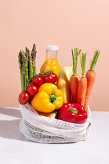 Raw colorful fresh vegetables in white mesh bag on table in hard light