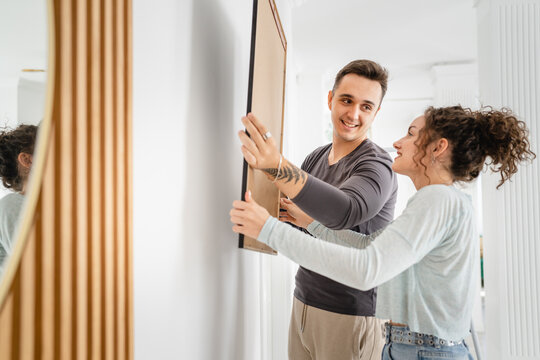 man and woman caucasian couple hanging painting on the wall at home
