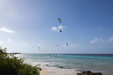 Sandy beach with turquoise water and kitesurfers on the horizon. Kitesurfing lessons.