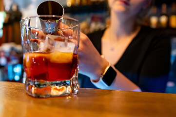 woman hand bartender making negroni cocktail. Negroni classic cocktail and gin short drink with sweet vermouth, red bitter liqueur in bar