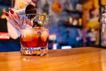 woman hand bartender making negroni cocktail. Negroni classic cocktail and gin short drink with sweet vermouth, red bitter liqueur in bar