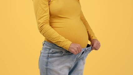 Close up shot of unrecognizable pregnant lady wearing oversize denim pants, showing her sporty figure during pregnancy