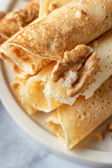 Rolled crepes or thin pancakes with honey and nuts on a white marble background close up. Maslenitsa or Pancake day traditional food concept