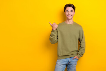 Photo of cheerful satisfied man beaming smile look indicate finger empty space isolated on yellow...