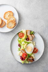 Caesar salad in modern linear feed with chicken, egg, tomatoes, lettuce and parmesan chips on gray table, top view, flat lay. Light diet, menu