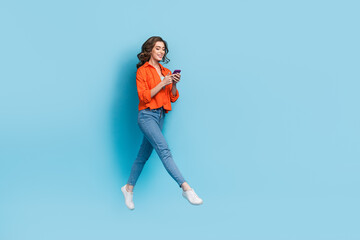Fototapeta na wymiar Full length photo of attractive woman flying walking chatting hold device dressed stylish orange garment isolated on blue color background