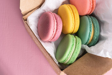 Cake macarons or macaroons in a gift box on a pink background, top view, pastel, colorful, almond cookies.