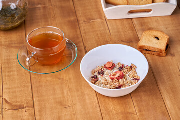 Tea in a glass cup on the wooden table oatmeal muesli in white plate.