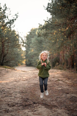 Obraz premium Little blonde girl dancing jumping on the sand in a pine forest