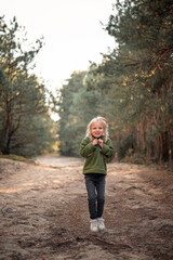 Little blonde girl dancing jumping on the sand in a pine forest