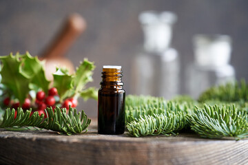 A dark bottle of essential oil with fir and holly branches