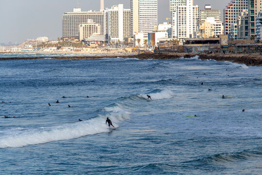 Surfers in distance in Tel Aviv and hotels or residential buildings next  to coastline in Tel Aviv . A little shadow of cloud on foreground