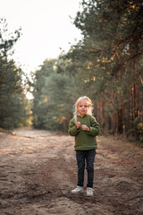 Fototapeta premium Little blonde girl dancing jumping on the sand in a pine forest